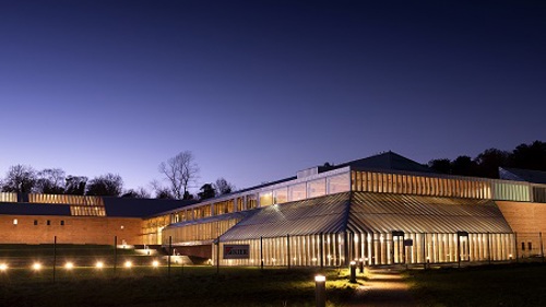 Lit-up exterior of the Burrell Collection at night, a large sandstone and glass museum building in a country park in Glasgow