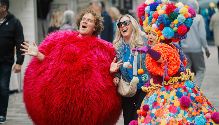 Costumed characters laugh alongside a person with blonde hair and blue jacket
