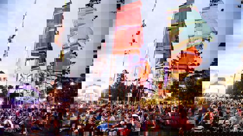 A large crowd at an outdoor music festival with large colourful flags throughout the site
