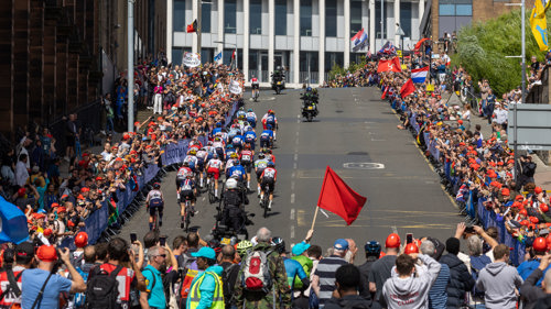 A large crowd watching an outdoor cycling event watching a group of professional cyclists climb a steep city street