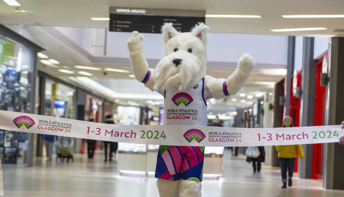 A Scottish Terrier mascot runs through a finish line promoting the 2024 World Athletics Indoor Championships in Glasgow