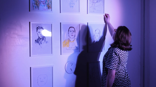 A person arranges portraits on a wall for an exhibition. 