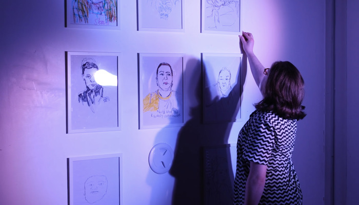 A person arranges portraits on a wall for an exhibition. 