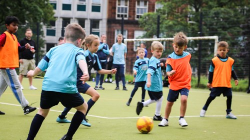 Two groups of young people wearing colourful bibs playing a football match on an outdoor pitch