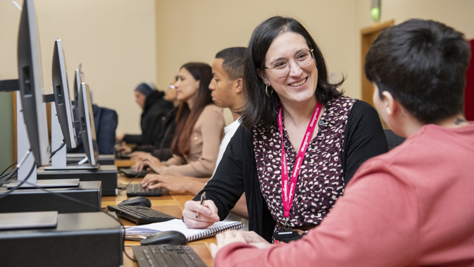 A Glasgow Life colleague wearing a rubine red lanyard while sitting at a computer next to a customer.