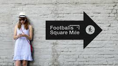  A person in a white summer dress, hat and sunglasses is leaning against a white wall and looking at their phone