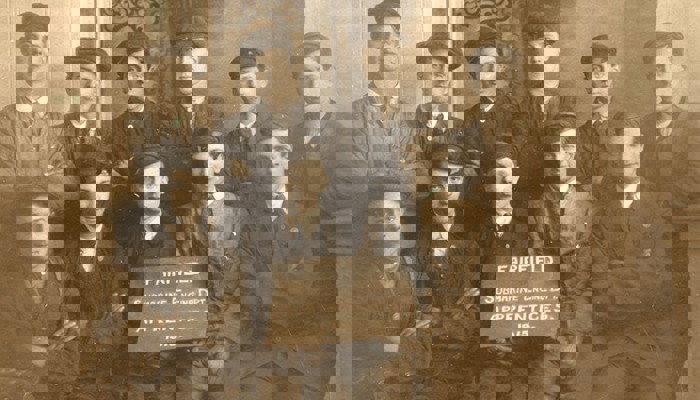 Black and white photo of 11 people sitting in dark uniforms, including hats and ties, holding a sign that says "Fairfield Submarine Engine Department Apprentices 1915"