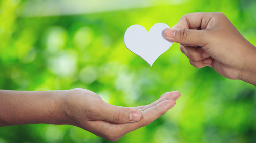 Close up on two hands. One is cupped to receive a white heart shape being held by the other