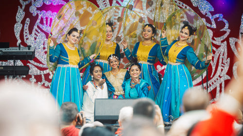 A group of dancers in colourful outfits performing on the main stage at the Glasgow Mela.
