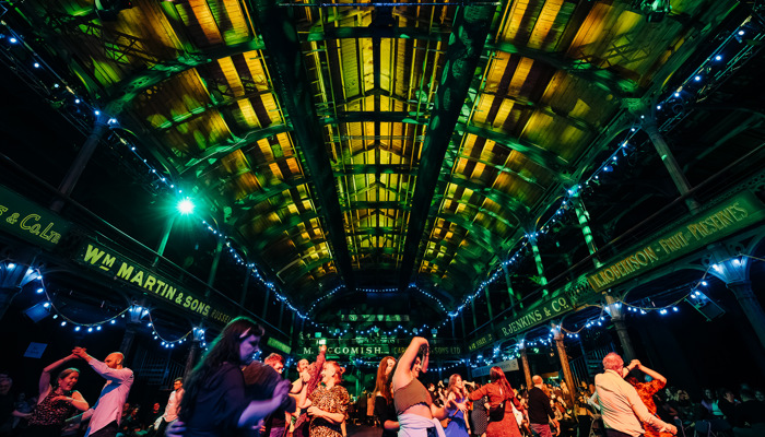 People are dancing during a ceilidh in a warmly lit live music venue 
