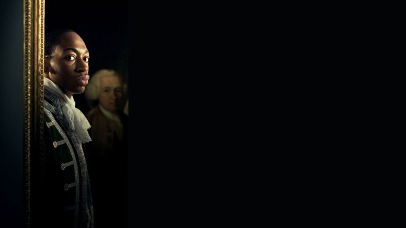 close up of boy looking at the screen with an oil painting of a man behind him