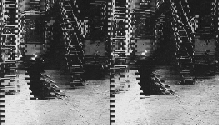 A black and white photograph of trams in a depot with ladders at each side and space underneath for maintenance checks.