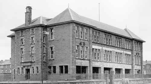 Black and white photo of Govan Parish Church Street Public School with bare tree branches coming in from the sides and children playing in the playground.
