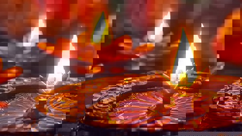 Two colourful metal Diwali oil lamps, lit on a table