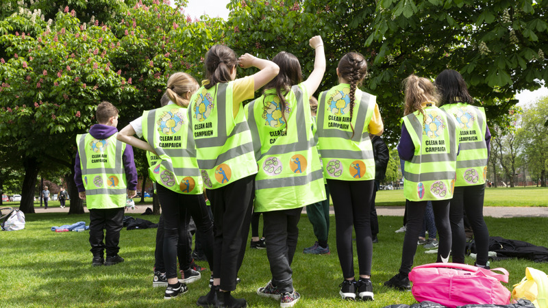 A group of children wear high vis vests with hand made logos, designs and messages relating to clean air on them
