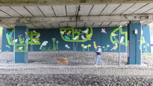A large blue and green mural showing nature in an underpass on a roadside.