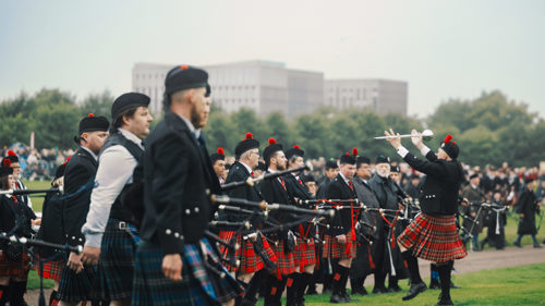 Pipers lined up in a row are dressed in kilts and holding bagpipes