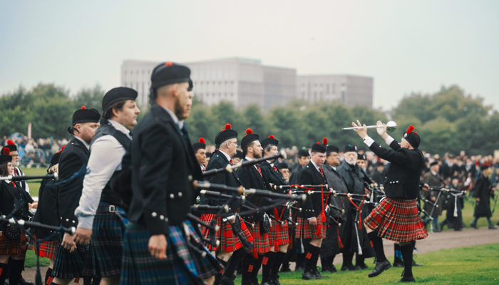 Pipers lined up in a row are dressed in kilts and holding bagpipes